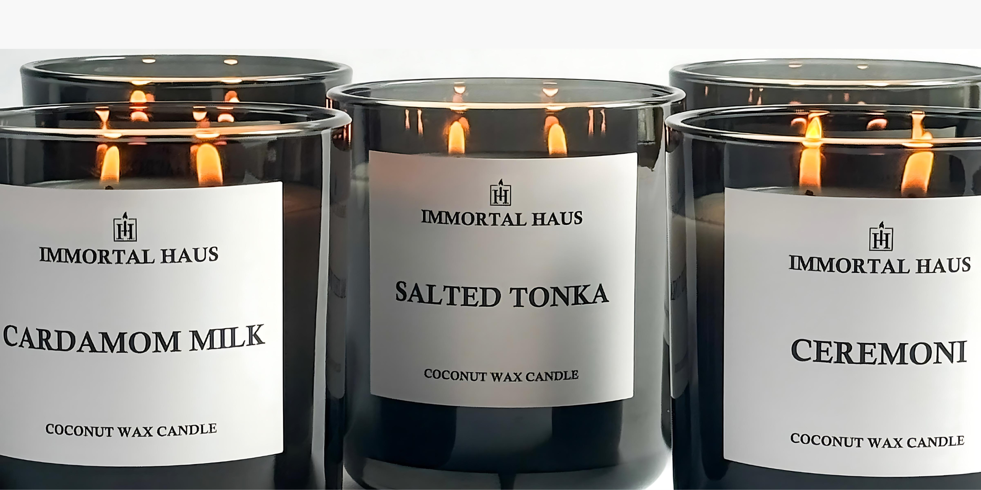Three Immortal Haus candles with lit flames on a white background